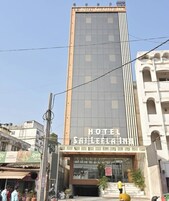 Un edificio de hotel alto con fachada moderna de vidrio y un letrero que dice 'HOTEL SAI LEELA INN'.