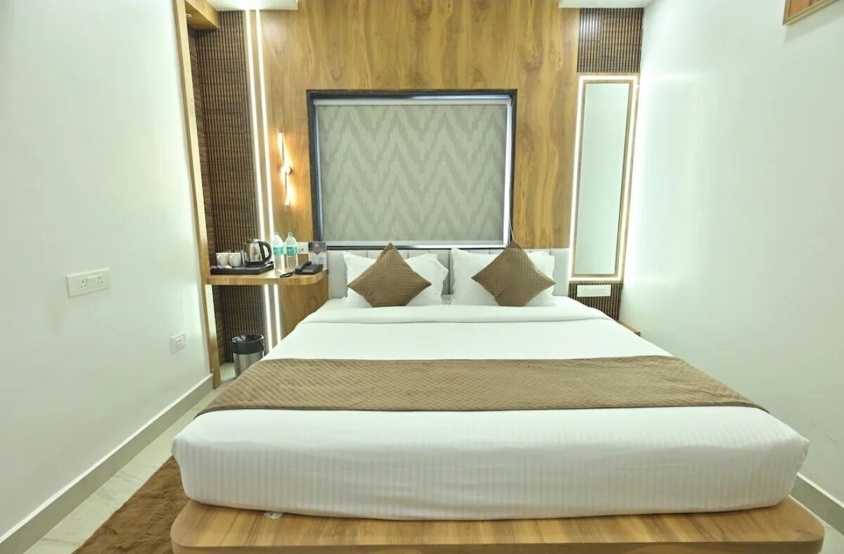 Ein Hotelzimmer mit einem großen Bett, einem hölzernen Kopfteil, einem Nachttisch mit Lampe und einem Spiegel.