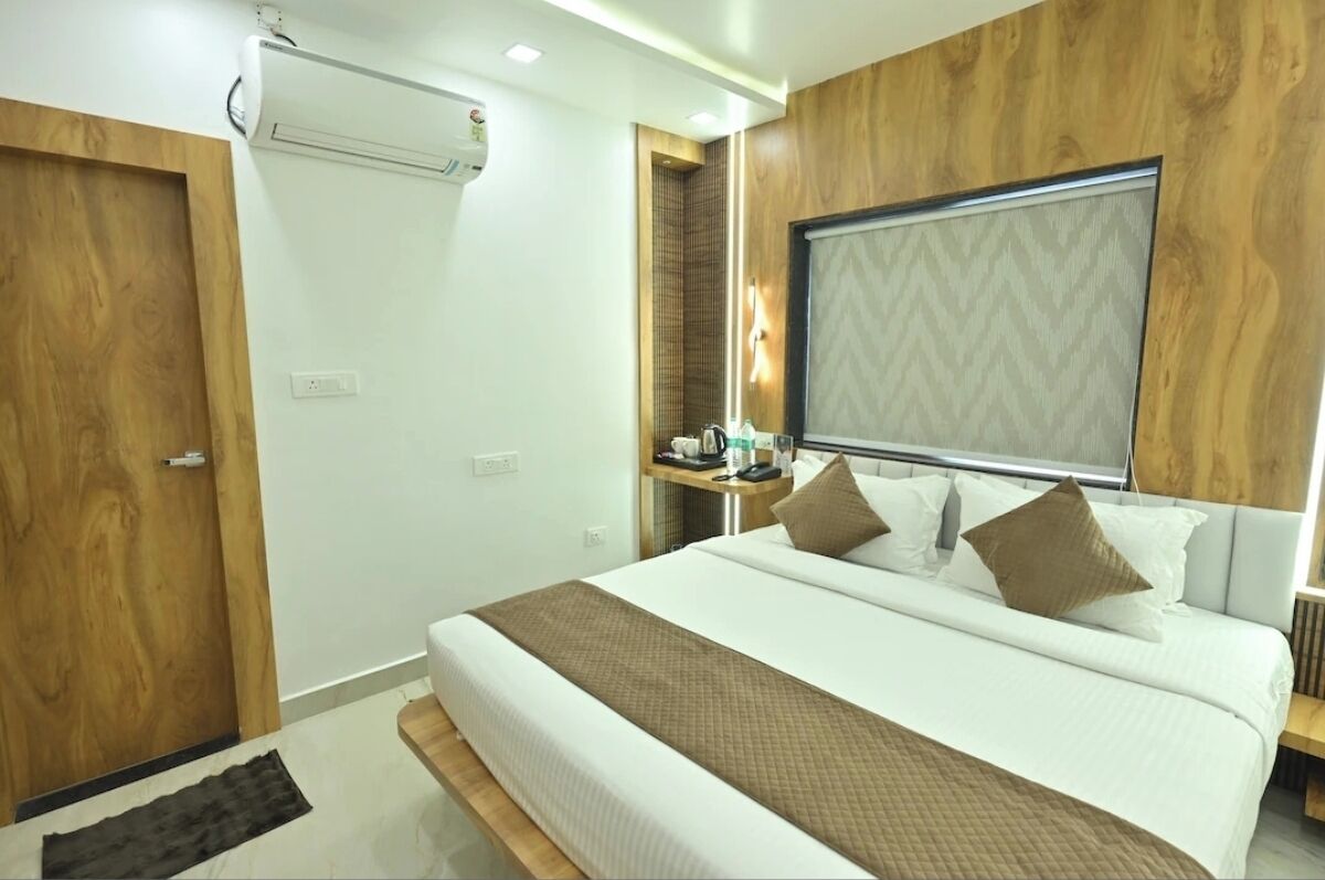 A modern hotel room with a large bed, wooden accents, a built-in heater, and a bedside table with a lamp.