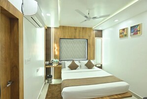A hotel room with a bed, a ceiling fan, an air conditioning unit, a nightstand, a window, and a wall-mounted artwork.