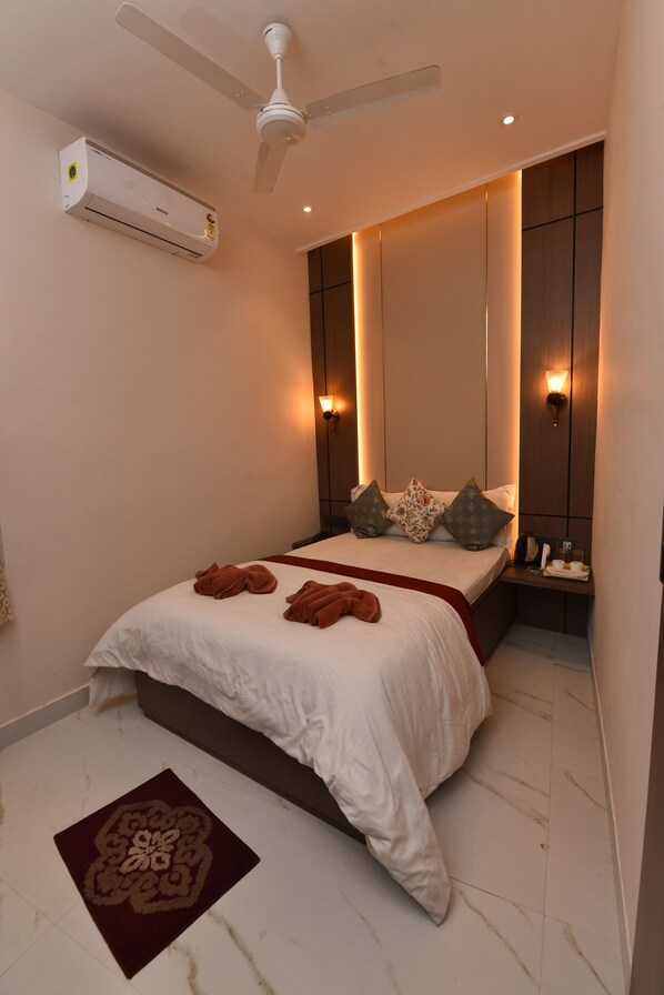 A bedroom with a bed, a ceiling fan, an air conditioner, bedside lamps, and a nightstand. - Basera Guest House (Kolkata)
