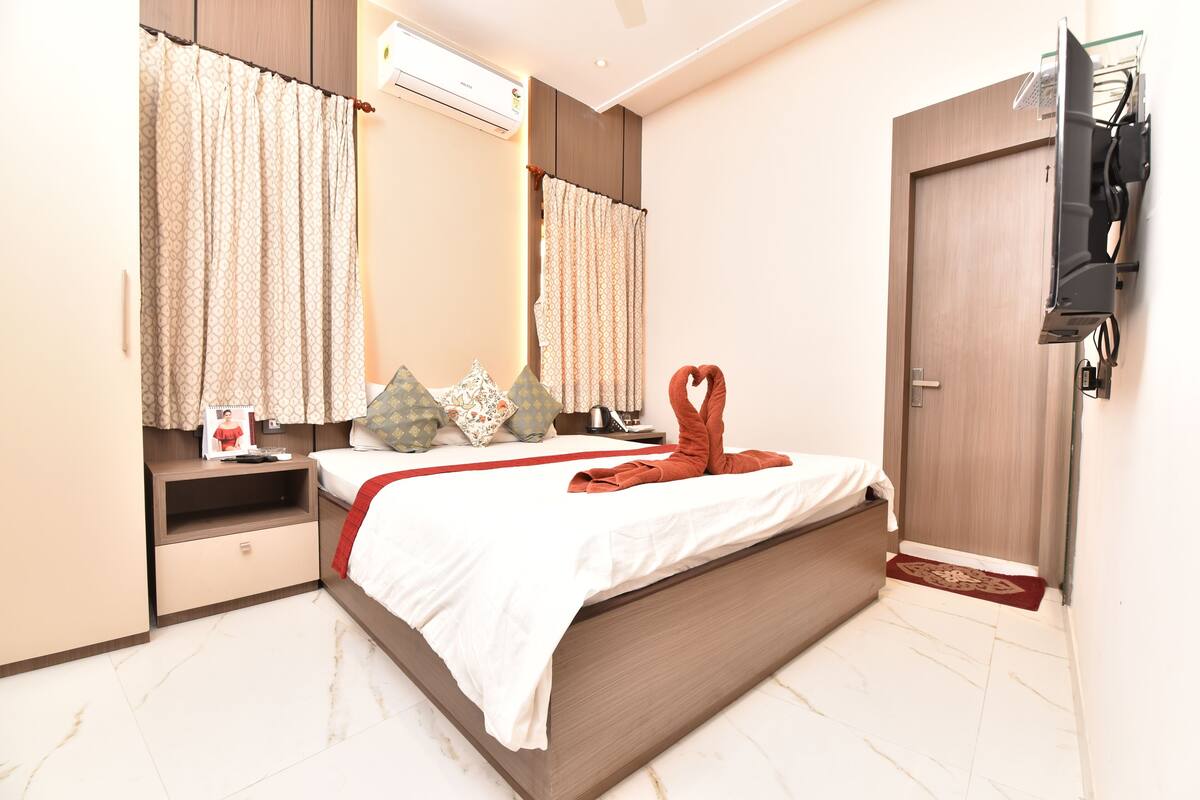 A hotel room with a bed, a nightstand, a TV mounted on the wall, and a door.