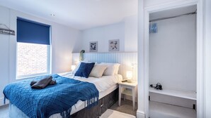 A bedroom with a bed, a nightstand, a window with a blue blind, and a walk-in closet. - Guestz at The Wellington (Blackpool)