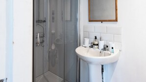 A bathroom with a glass-enclosed shower, a white sink with toiletries, and a wooden-framed mirror on the wall. - Guestz at The Wellington (Blackpool)
