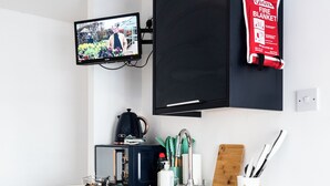A compact kitchen with a built-in microwave, a coffee maker, and a sink. A television is mounted on the wall, and a fire blanket is visible. - Guestz at The Wellington (Blackpool)