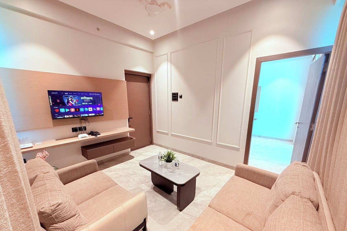 A modern living room with a flat-screen TV, a sofa, a coffee table, and a sliding door to a balcony.