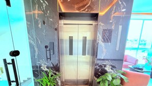 An elevator with a marble wall, a potted plant, and a red couch in the lobby. - PURPLE LOTUS SUITES (Khalapur)