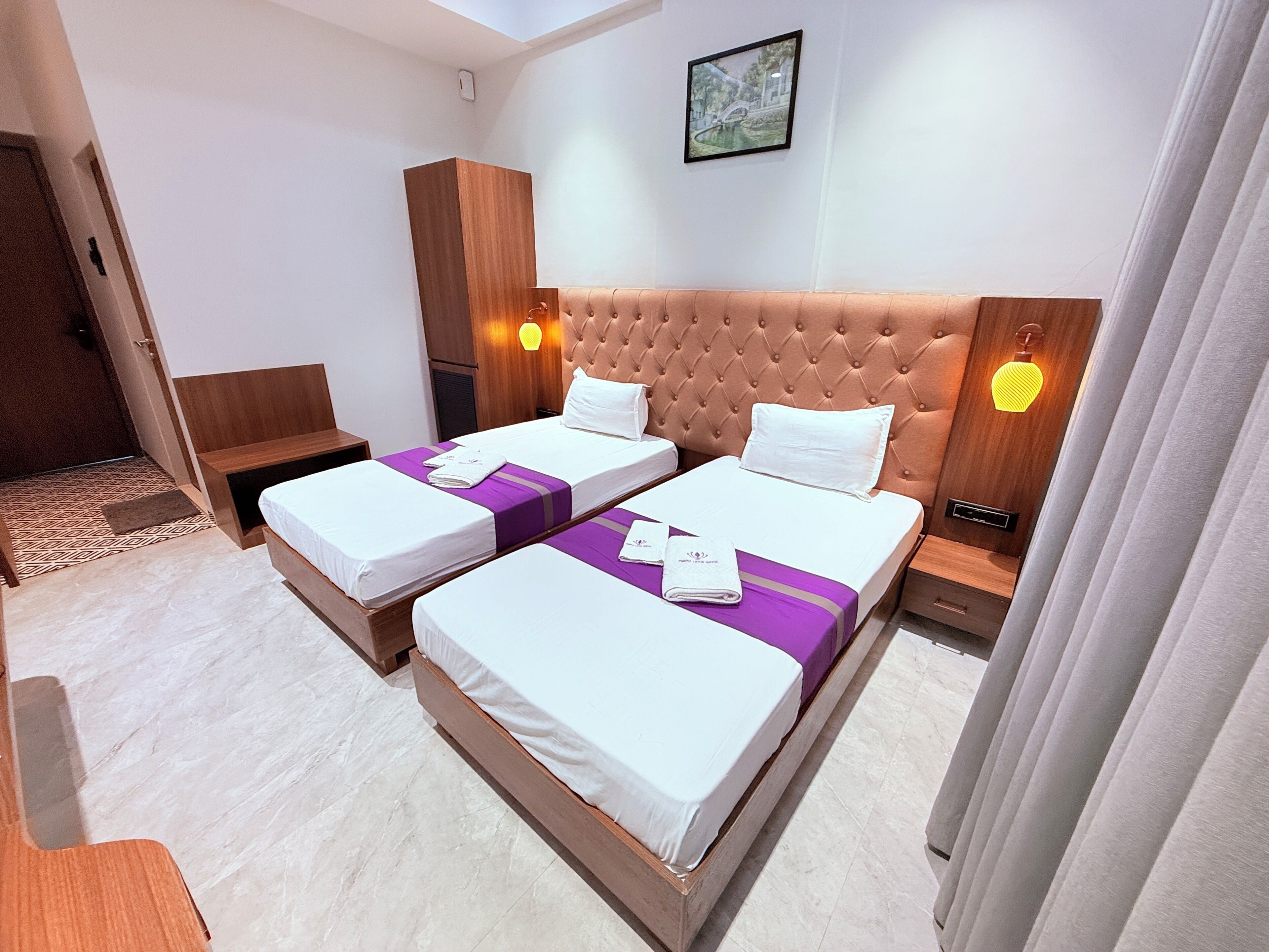 A hotel room with two beds, a wooden headboard, a wall-mounted picture, and a bedside table with a lamp.