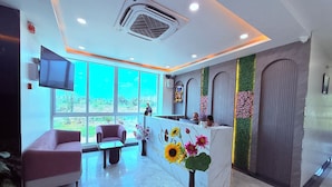 A reception area with a marble counter, a television, and a large window offering a view of greenery. - PURPLE LOTUS SUITES (Khalapur)
