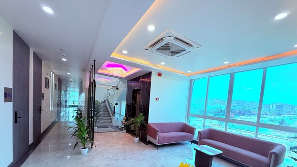 A modern lobby with a marble floor, a staircase, a reception desk, and large windows offering a city view. - PURPLE LOTUS SUITES (Khalapur)