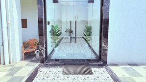 A modern entrance with a glass door, a checkered floor, and a small bench outside. - PURPLE LOTUS SUITES (Khalapur)