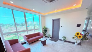 A modern lobby with a red sofa, a small table, potted plants, and a door. - PURPLE LOTUS SUITES (Khalapur)