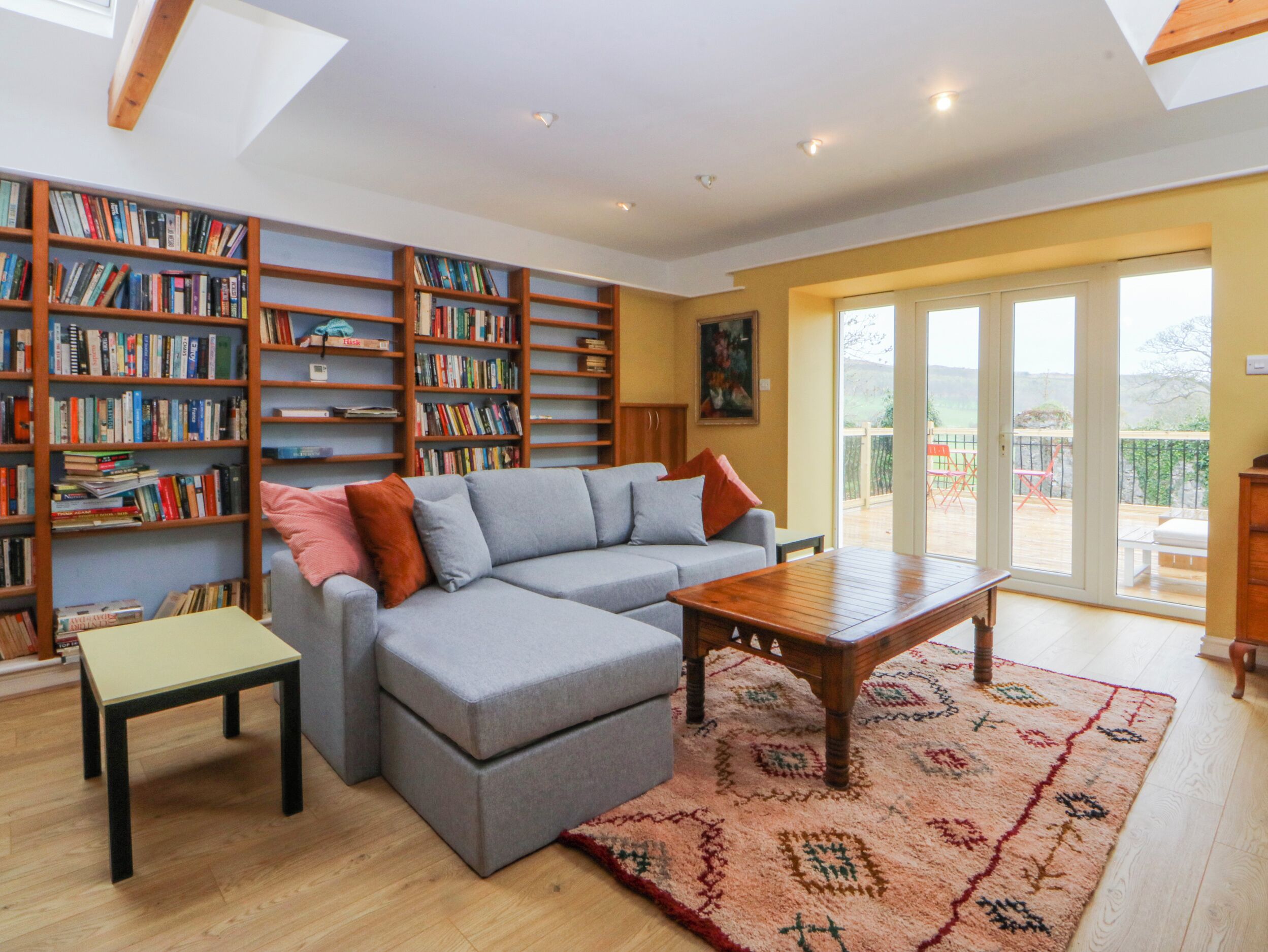 A living room with a grey sofa, a wooden coffee table, a small table, and a bookshelf filled with books.