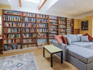 Ein geräumiges Wohnzimmer mit einer großen Bücherwand, einer grauen Couch mit Kissen, einem kleinen Tisch und einem gemusterten Teppich.