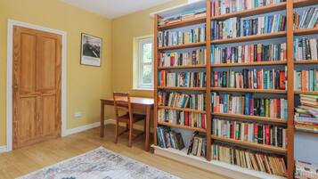 A room with a wooden bookshelf filled with books, a wooden desk, a chair, a wooden door, and a window.