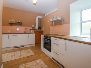 Eine Küche mit weißen Schränken, einer Holzarbeitsplatte, einem eingebauten Backofen und einem Fenster.