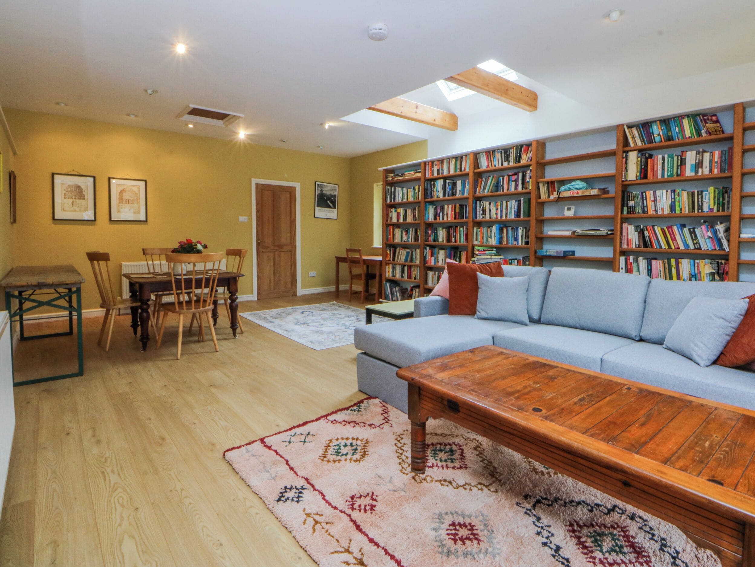 Uma sala de estar com sofá, mesa de centro, piso de madeira, estantes de livros e um espaço de jantar com cadeiras e mesa.