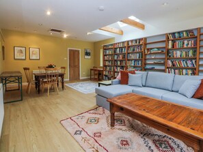 Ein Wohnzimmer mit einer Couch, einem Couchtisch, Holzboden, Bücherregalen und einem Essbereich mit Stühlen und einem Tisch.
