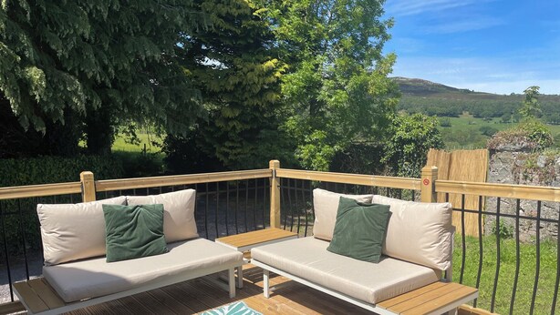 A deck with two beige sofas, a wooden table, and a patterned rug. - Inglewood Bach (Conwy)