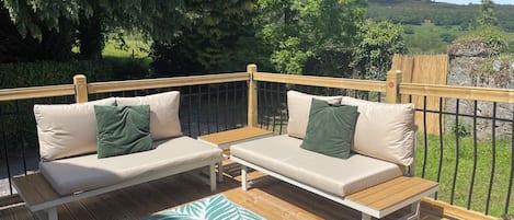 A deck with two beige sofas, a wooden table, and a patterned rug.