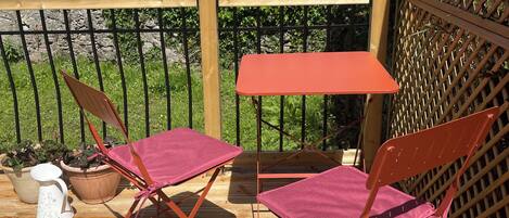 A wooden deck with two folding chairs and a small table, surrounded by a wooden fence and greenery.