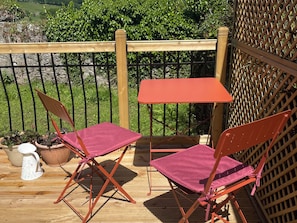 A wooden deck with two folding chairs and a small table, surrounded by a wooden fence and greenery. - Inglewood Bach (Conwy)