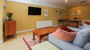A spacious living area with a wooden coffee table, a grey sofa, a dining table with chairs, and a TV mounted on the wall. - Inglewood Bach (Conwy)