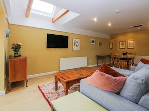 A spacious living area with a wooden coffee table, a grey sofa, a dining table with chairs, and a TV mounted on the wall. - Inglewood Bach (Conwy)