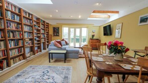 A spacious living room with a large bookshelf, a dining area with a wooden table, and a sofa. - Inglewood Bach (Conwy)