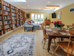 A spacious living room with a large bookshelf, a dining area with a wooden table, and a sofa. - Inglewood Bach (Conwy)