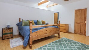 A bedroom with a wooden bed, a dresser, a mirror, and a door. - Inglewood Bach (Conwy)