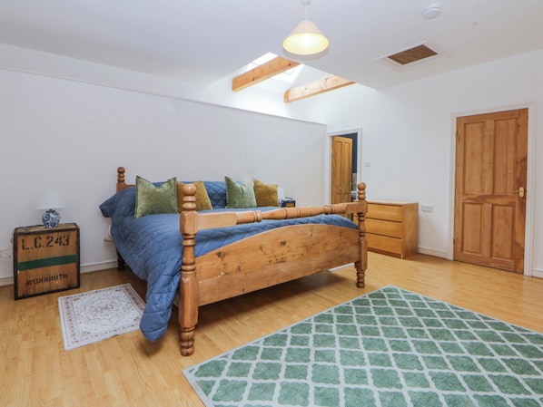 A bedroom with a wooden bed, a dresser, a mirror, and a door. - Inglewood Bach (Conwy)