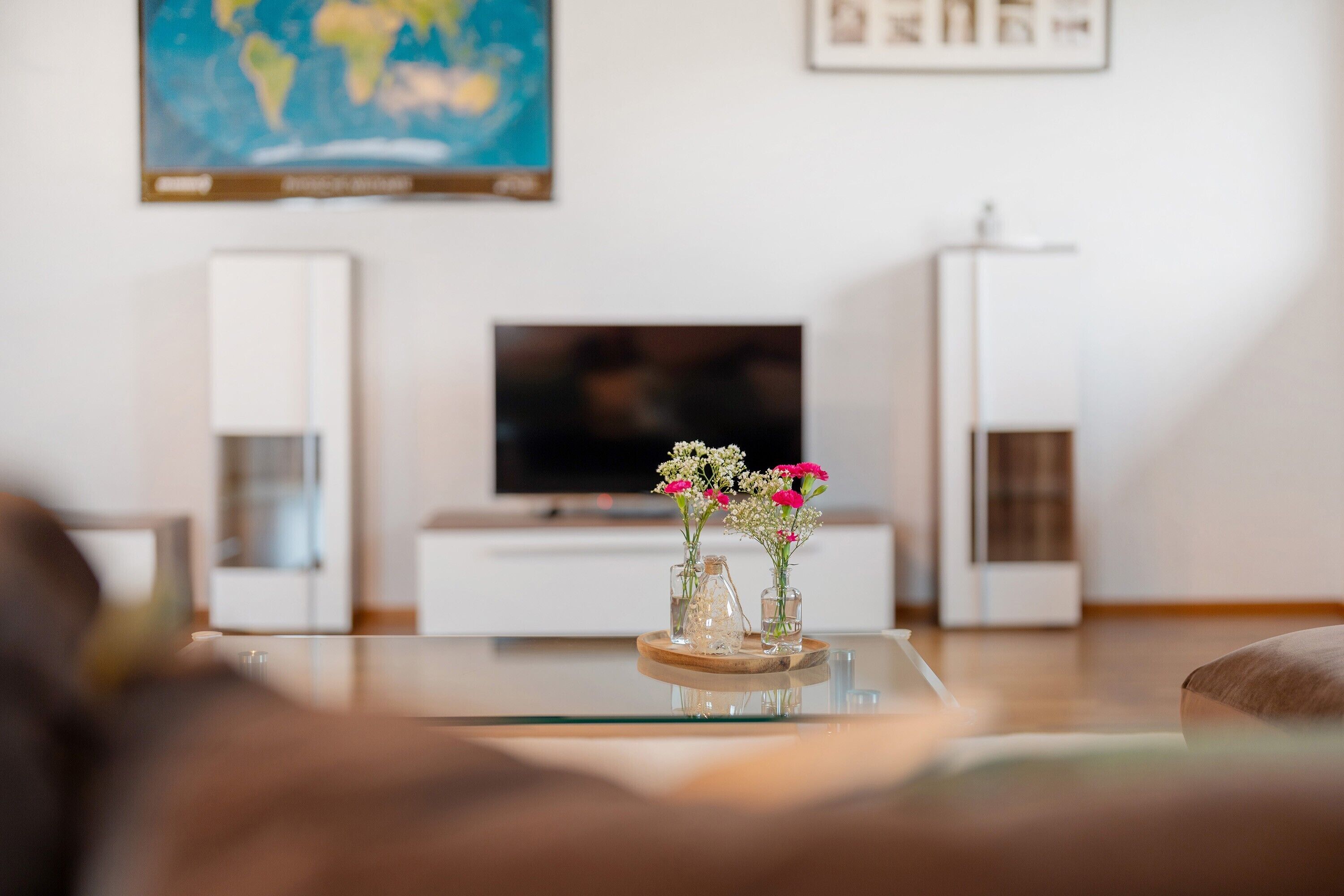 Un salon moderne avec une table basse en verre, un téléviseur à écran plat et des vases décoratifs ornés de fleurs.