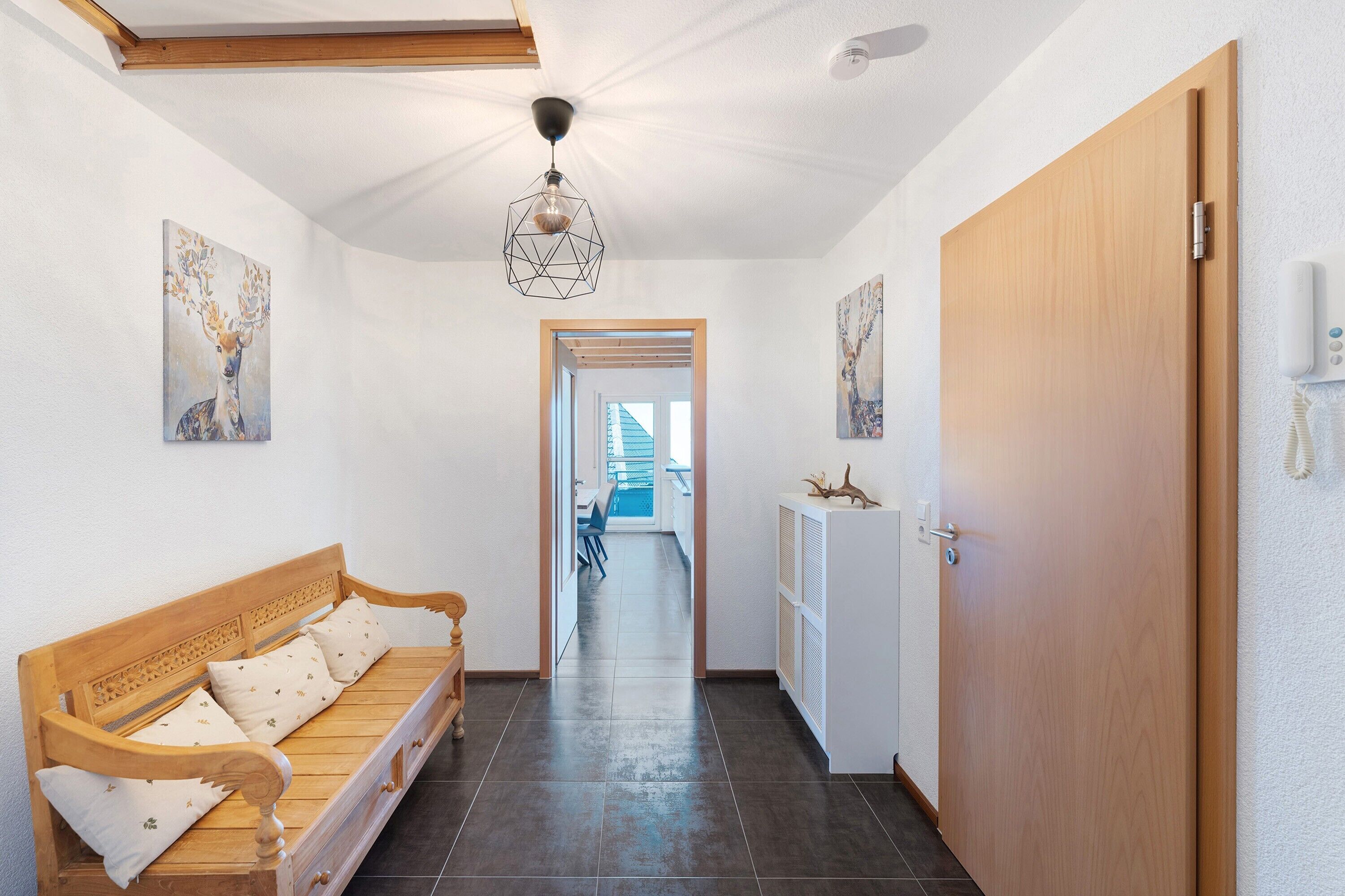 Un couloir avec un banc en bois, un luminaire au plafond et une porte.