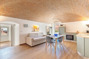 Ein modernes Interieur mit Ziegeldecke, einem Essbereich mit Tisch und Stühlen, einer Couch und einer Küche mit Geräten.