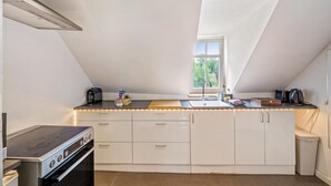 A modern kitchen with a gas stove, built-in oven, white cabinets, a window, and a countertop with various appliances.