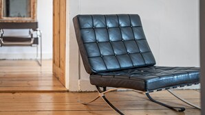 A black leather chair with a cushioned seat and backrest, positioned on a wooden floor with a visible door and a mirror in the background.