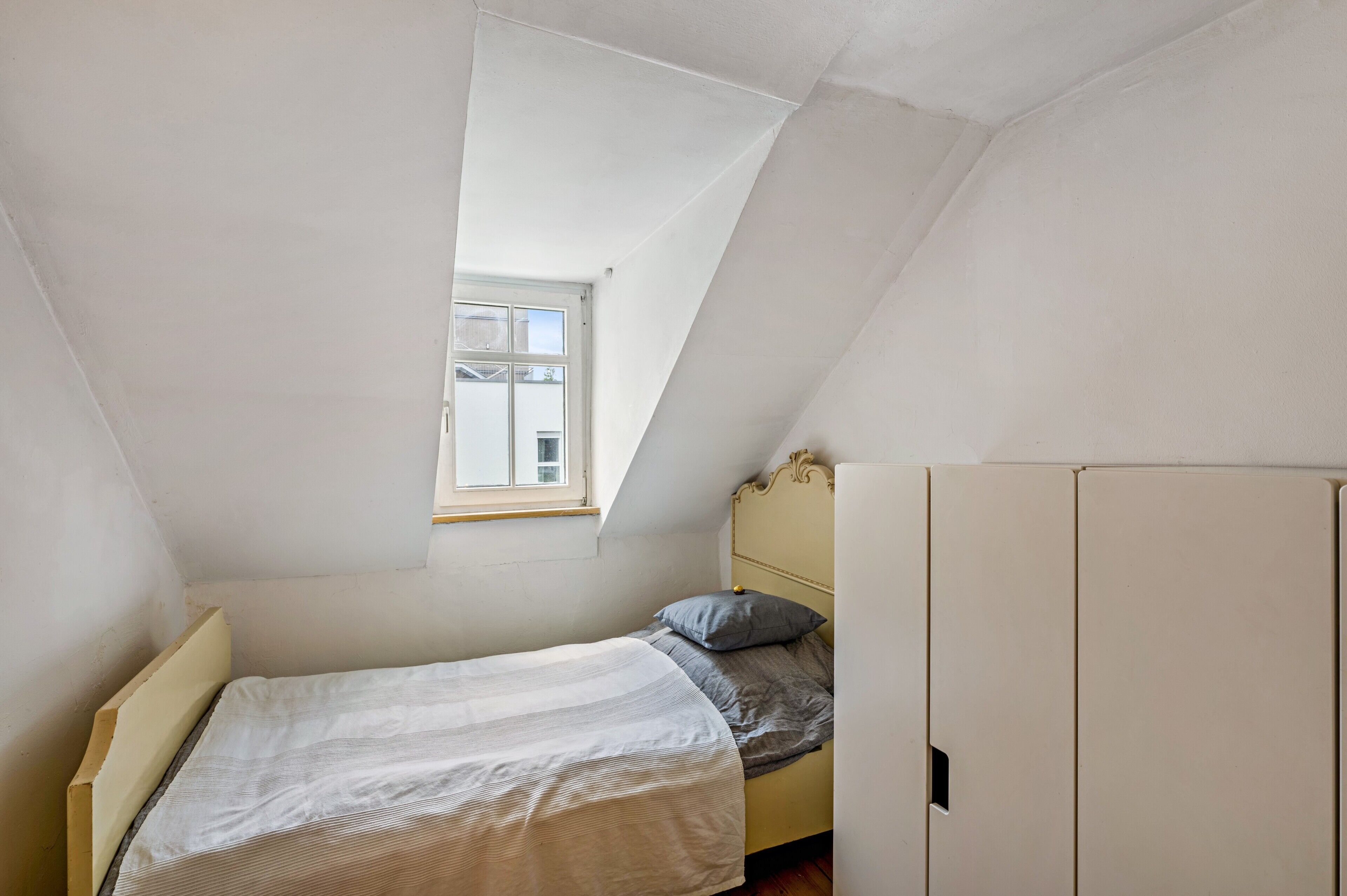 Een kleine kamer met een enkel bed, schuine plafond en een raam.