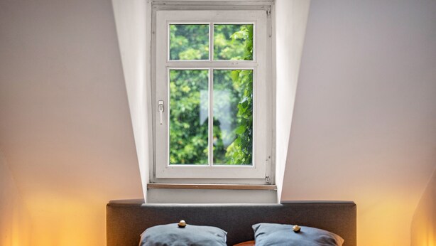 A bedroom with a bed, pillows, a window, and two wall-mounted lamps.