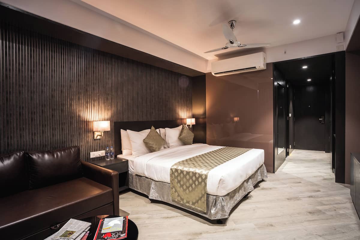 A modern hotel room with a bed, a sofa, a nightstand, and an air conditioning unit.