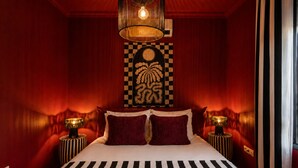 Quarto com uma cama grande, duas luminárias de cabeceira, uma obra de arte com padrão xadrez e um lustre.