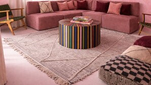 Uma sala de estar em tons de rosa, com sofá modular, mesa de centro redonda e duas luminárias pendentes.