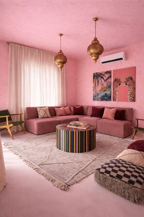Ein salon in Rosa mit einem Ecksofa, einem runden Couchtisch und zwei Pendelleuchten.