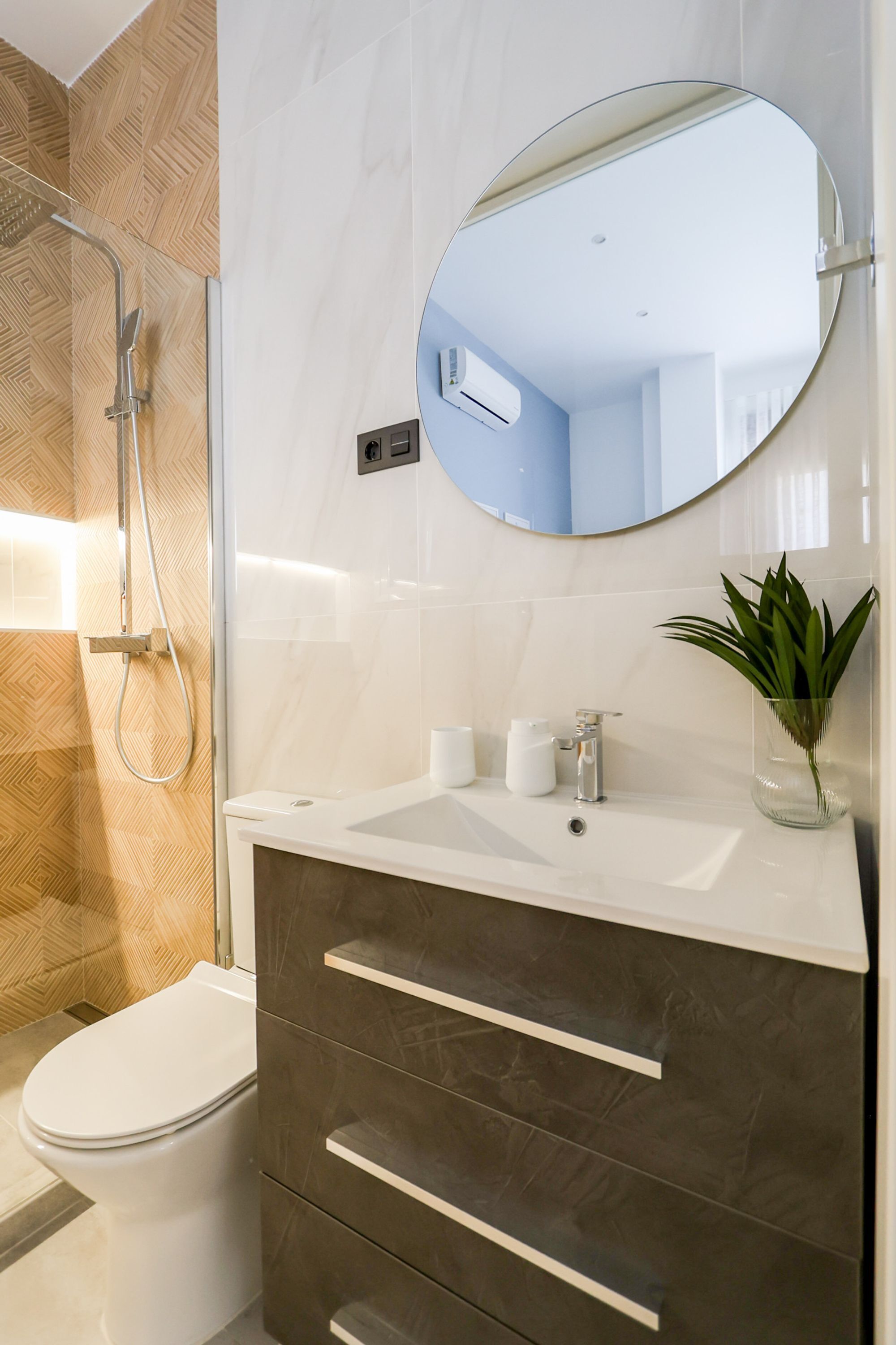 Une salle de bain moderne équipée d’une douche, de toilettes, d’un meuble-lavabo avec des tiroirs, d’un miroir et d’une plante en pot.