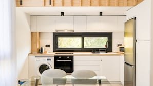 A modern kitchen with a built-in oven, microwave, and refrigerator, a glass dining table with chairs, and a window above the sink. - AS EXT Fgrl Rferial 4 (Fuengirola)