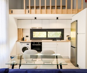 Eine moderne Küche mit Einbauofen, Mikrowelle und Kühlschrank, ein Glastisch mit Stühlen sowie ein Fenster über der Spüle.