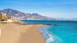 Una playa costera con una montaña al fondo, cielo despejado y mar tranquilo.