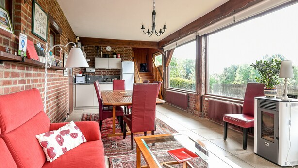 A cozy room with a red sofa, a dining table, and chairs. There's a kitchen area with a fridge and a stove. The room has large windows and a view of greenery outside. - La Bulle Mathusalem Guest Room on the Opal Coast, 8 km from Berck, 15 km from Le Touquet (Verton)