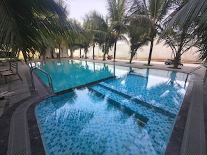A swimming pool with tiled edges, surrounded by palm trees and lounge chairs. - Greenway Retreat Resort (Vanur)