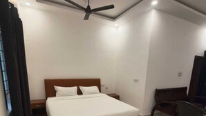 Une chambre à coucher avec un lit, un ventilateur de plafond, un bureau avec des chaises et une fenêtre avec des rideaux.